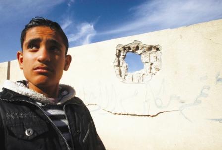 شاب فلسطيني أمام جدار مدرسة تعرض لقصف جوي إسرائيلي في غزة أمس الخميس